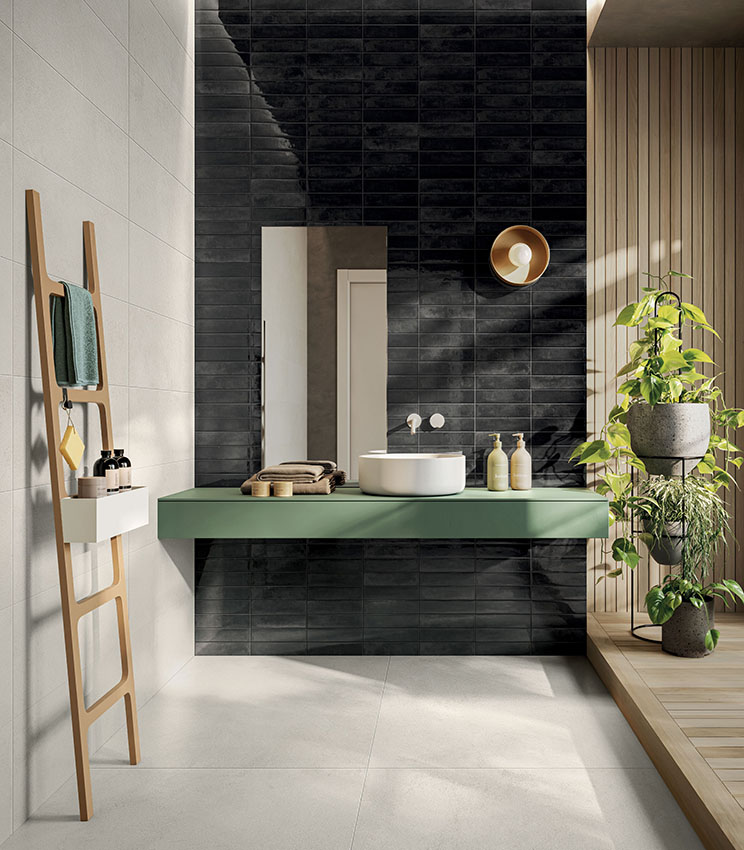 Salle de bains contemporaine avec des surfaces des collections La Matière Talc et Workshop Core, caractérisée par un mur sombre brillant, des surfaces claires, un meuble vasque vert suspendu, des détails en bois et de nombreuses plantes baignées de lumière naturelle.