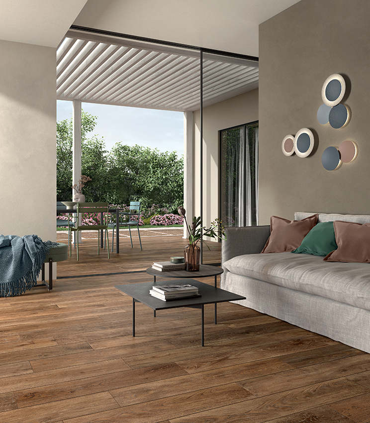 Salon contemporain avec un sol de la collection Kairos Zoi, caractérisé par des surfaces effet bois aux tons chauds, un grand canapé clair, des tables basses et un accès direct à une terrasse aménagée donnant sur la verdure.