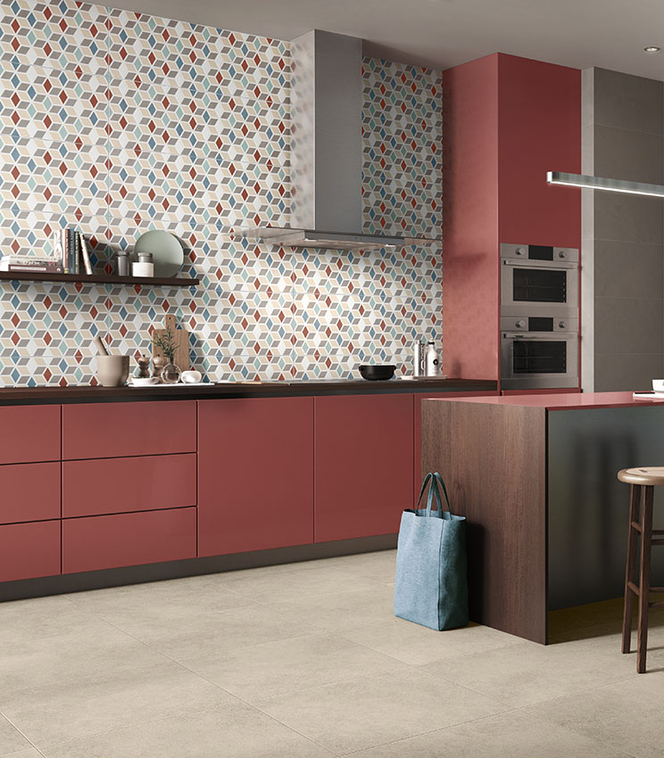 Cuisine contemporaine avec des surfaces des collections Even Dove, Optical Terzofuoco et Context Square, caractérisée par un revêtement mural géométrique multicolore, des meubles couleur terre cuite, un plan de travail sombre, un îlot central et un sol clair.