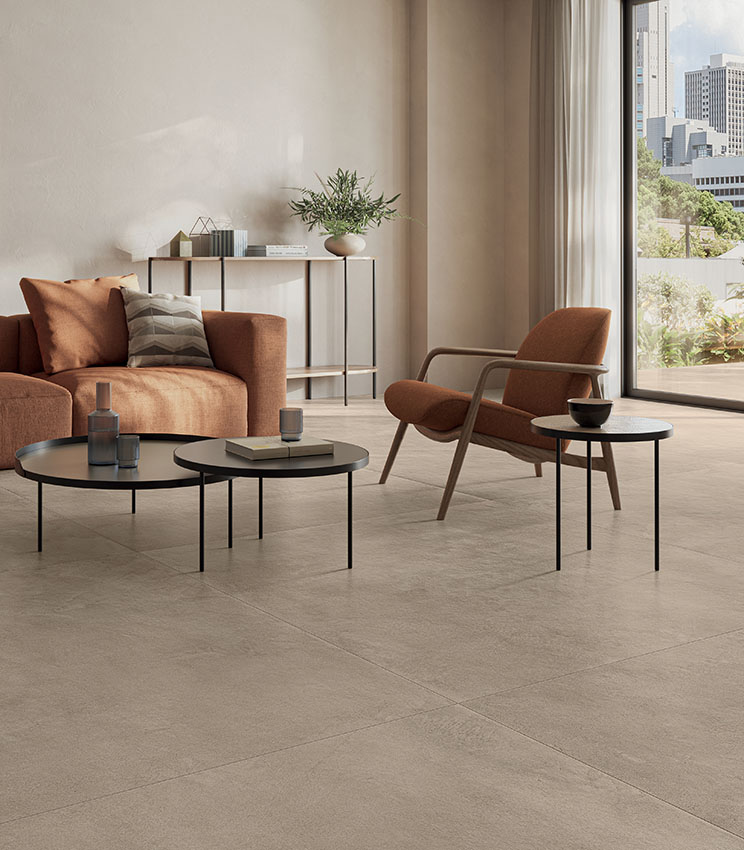 Salon moderne aux tons chauds et terreux, avec porte-fenêtre donnant sur la terrasse et sol en grès cérame effet béton couleur sable.