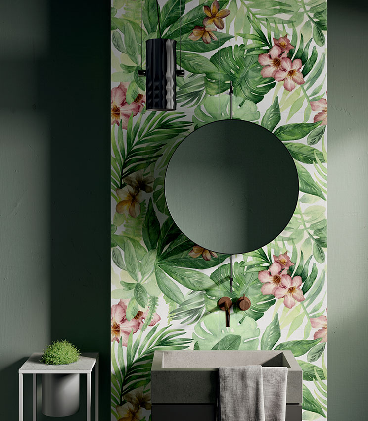 Vue de face d’un mur de lavabo revêtu de grès cérame effet papier peint à motifs végétaux, avec miroir rond et vasque carrée.