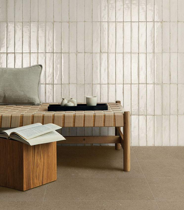 Espace moderne et apaisant avec banc en bois et assise tressée, mur revêtu de carreaux en céramique brillante couleur ivoire et sol en grès cérame aux tons naturels.