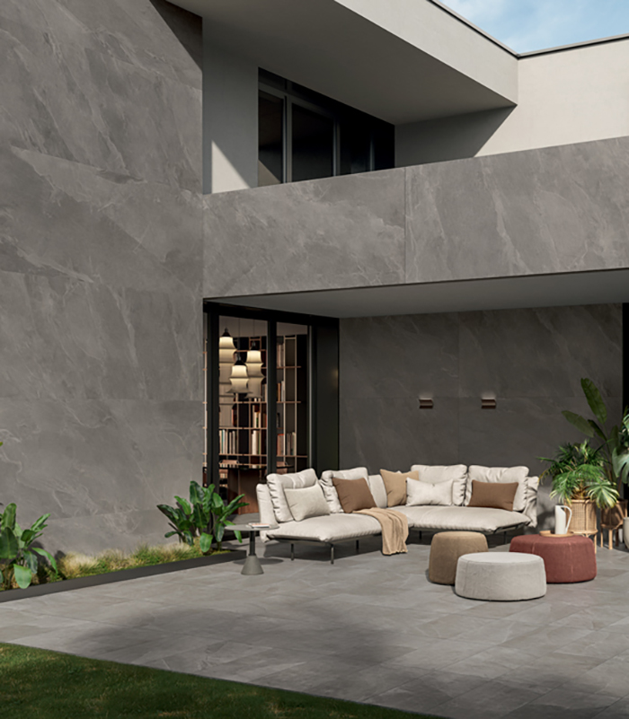 External view of a modern villa with rigorously geometric design, partially clad in large stone-effect ceramic slabs, featuring a furnished patio paved with 20-mm-thick stone-effect porcelain stoneware.
