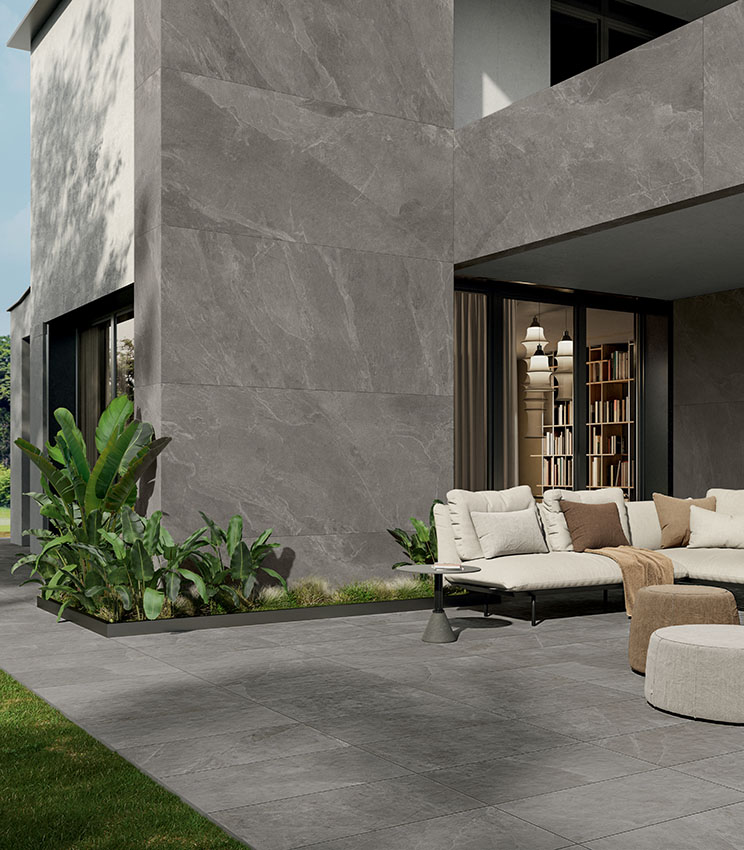 Vue extérieure d’une villa au design moderne et résolument géométrique, partiellement revêtue de grandes dalles céramiques effet pierre, avec patio aménagé et sol en grès cérame effet pierre de 20 mm d’épaisseur.