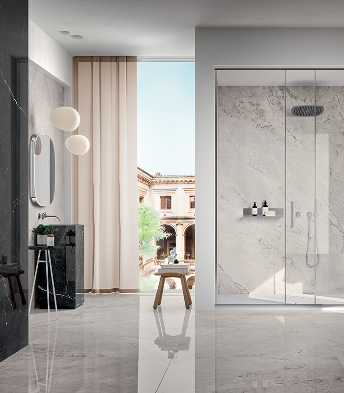 Elegant, bright bathroom with floors and walls, including a spacious shower, covered in white marble-effect porcelain stoneware. On the left, a section is covered in black marble-effect porcelain stoneware, including the freestanding sink.