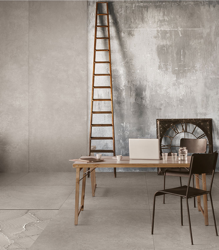 Espace de bureau de style industriel avec sol effet béton, murs texturés, escalier en bois et mobilier minimaliste en bois et métal.