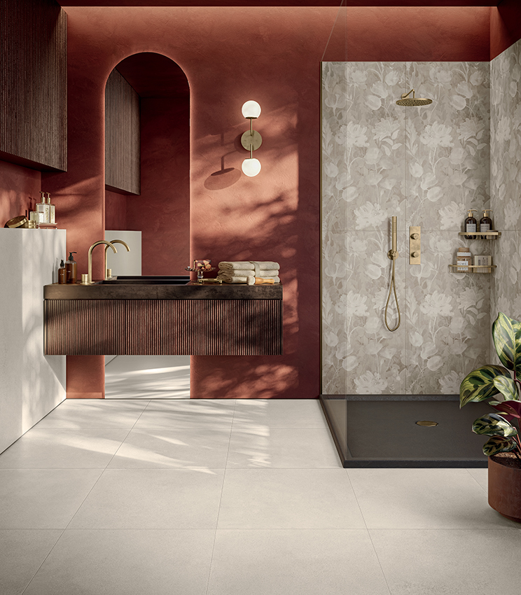 Salle de bains contemporaine à l’atmosphère chaleureuse et matérielle, habillée de surfaces de la collection Formula de Panaria Ceramica. Form Cotton Naturale crée une base neutre, tandis que le décor floral Garden Naturale caractérise l’espace douche et contraste avec élégance avec les murs couleur terre cuite et le mobilier foncé.