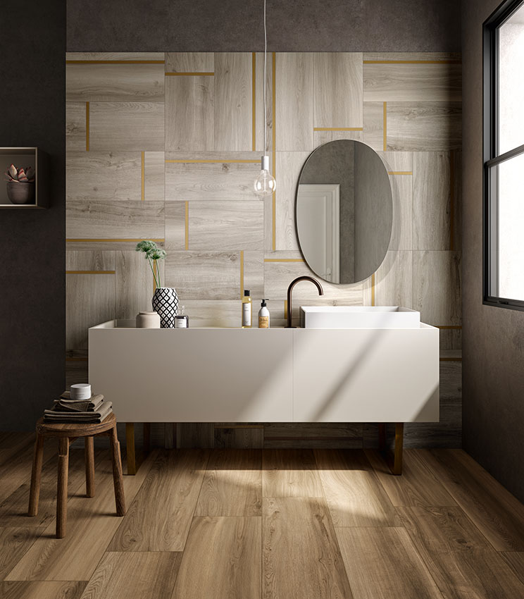 Vista frontale della parete lavabo di un bagno moderno, con pavimento in doghe di legno ceramico e rivestimento in gres porcellanato decorativo effetto legno con l'inserimento di listelli di ottone.