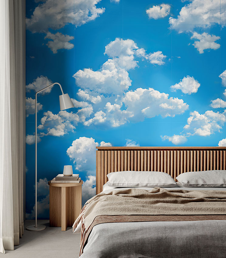 Chambre contemporaine avec un revêtement mural décoratif de la collection Glam Flow, représentant un ciel bleu avec de grands nuages blancs. La pièce est aménagée avec un lit à tête de lit en bois rainuré, du linge de lit aux tons neutres, une table de chevet en bois et un lampadaire blanc.
