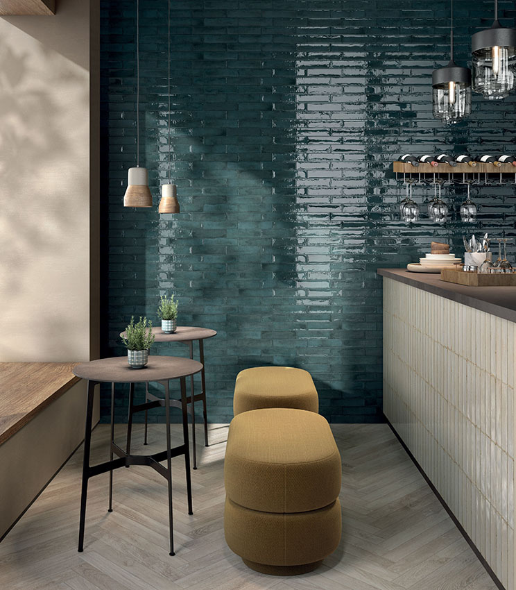 Coin bar contemporain avec des surfaces des collections Workshop Berry, Workshop Opal et Kairos Imera, caractérisé par un mur vert pétrole brillant, un comptoir revêtu dans des tons clairs, un sol effet bois et un mobilier compact avec des tabourets rembourrés et des tables hautes.
