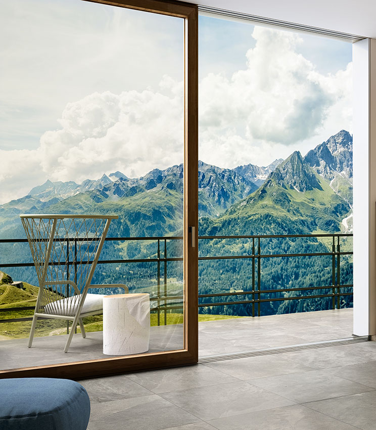 Vue au ras du sol du dallage extérieur et de la porte-fenêtre d'une chambre. Sols extérieur et intérieur assortis, en grès cérame effet pierre de couleur grise