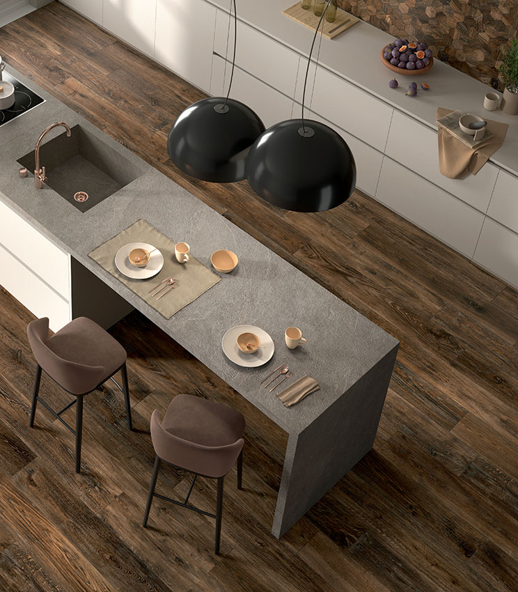 Vue de dessus d'une cuisine moderne avec îlot bar-dînette habillé de dalles de grès effet pierre gris clair et sol en lames foncées de grès cérame effet bois