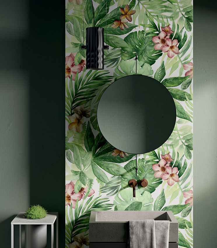 Salle de bains contemporaine avec un revêtement mural décoratif de la collection Glam Rainforest, caractérisé par un motif tropical de grandes feuilles vertes et de fleurs roses. L’espace comprend des murs vert foncé, une vasque aux lignes géométriques, un miroir rond, une robinetterie murale et une suspension noire.