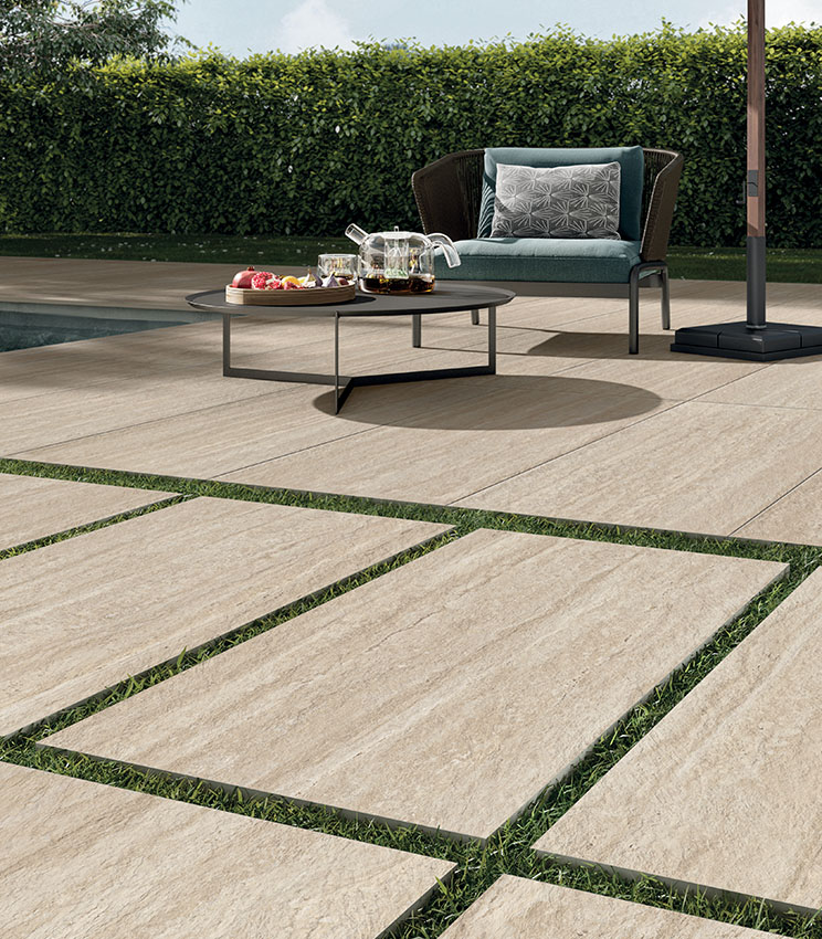 Vue en quasi rase-mottes d'un revêtement de sol extérieur en grès cérame 20 mm effet travertin devant une piscine | Collection Perpetual Travertino de Panaria Ceramica