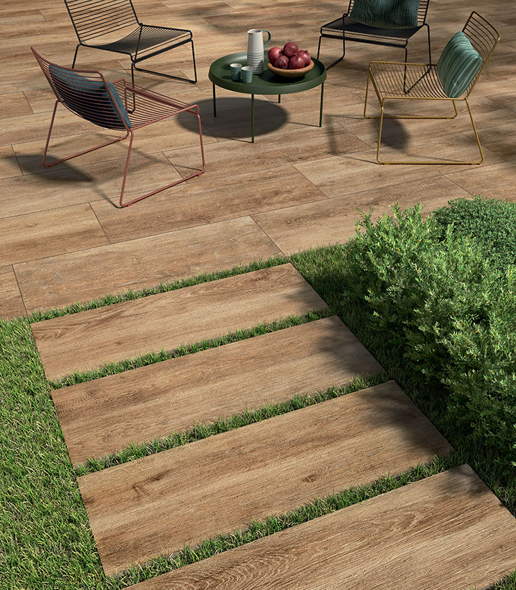 Vue d'un patio avec des chaises modernes en fil métallique et un sol en grès cérame 20 mm effet bois posé avec colle. Au premier plan, une allée de lames céramiques outdoor posées à sec sur gazon | Collection Kairos de Panaria Ceramica