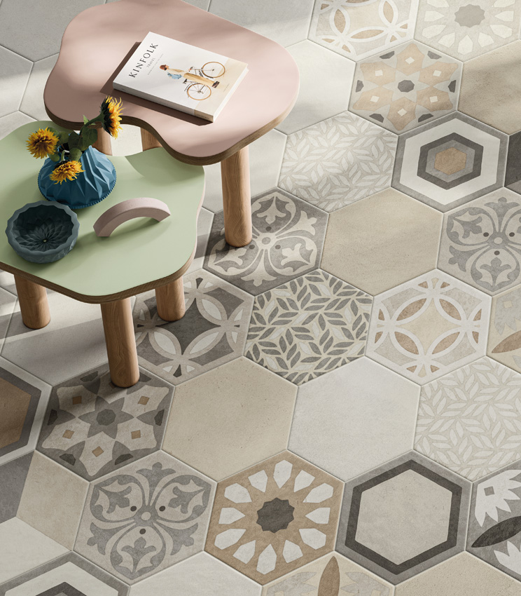 Vue en plongée d'un sol en grès cérame effet béton clair au format hexagonal avec deux petites tables basses colorées et une large portion de décors à motifs géométriques et de feuillage typiques des carreaux hexagonaux artisanaux.