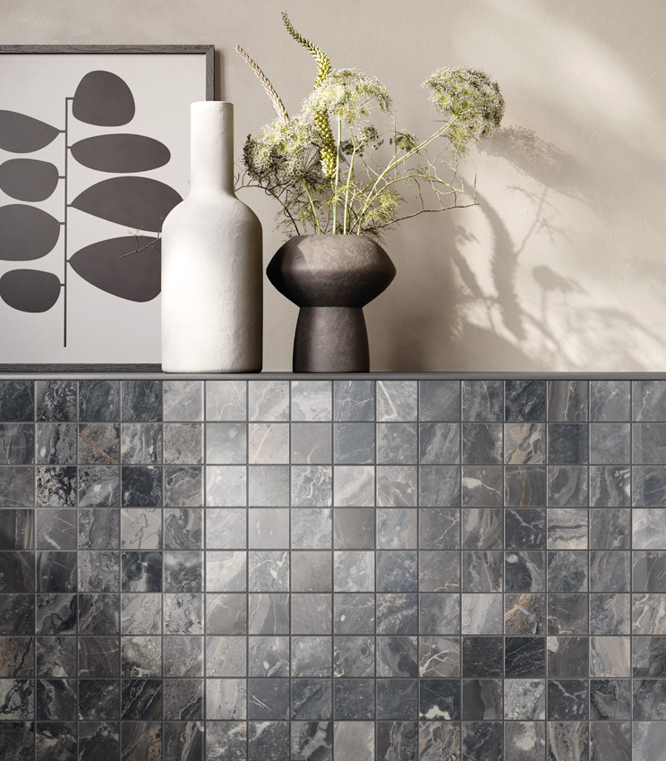 Vue rapprochée et frontale d'un muret avec une étagère sur laquelle reposent deux vases et un tableau abstrait. Le muret est habillé d'une mosaïque céramique effet marbre sombre tandis que le reste du mur est peint en ivoire.