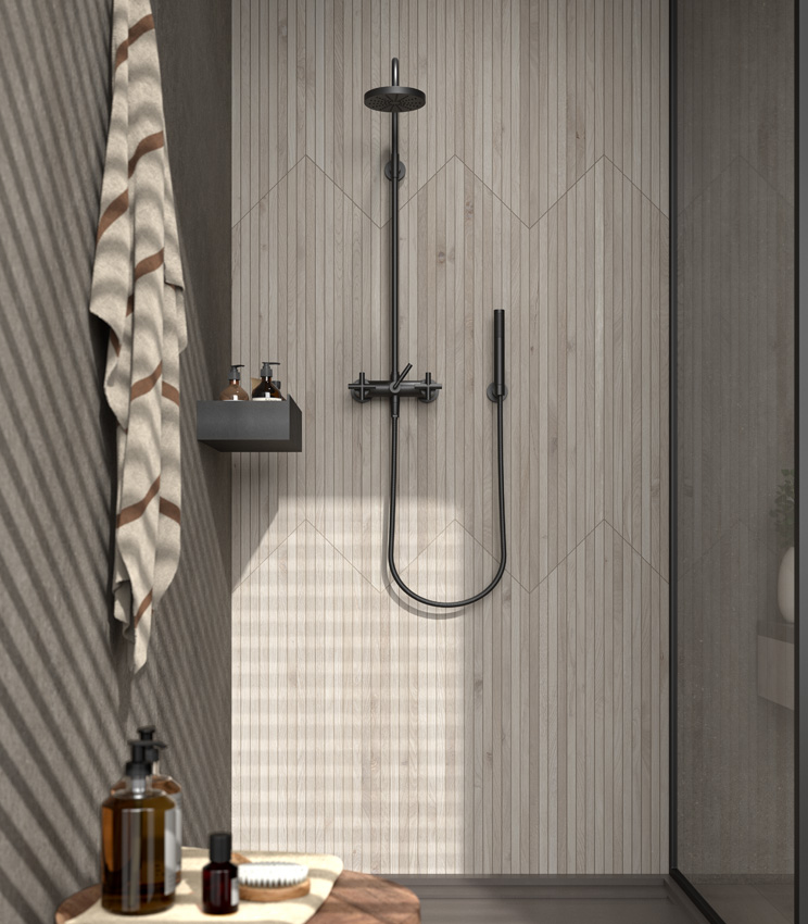 Vue frontale d'un angle de douche avec le mur de robinetterie habillé de fines baguettes en grès cérame effet bois de couleur claire, en contraste avec le mur adjacent et le receveur de douche sombres.