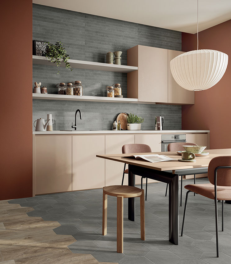Cuisine contemporaine avec un revêtement mural gris à effet linéaire et un sol géométrique, aménagée avec des meubles beige, des murs couleur terre cuite, une table à manger avec des chaises rembourrées et une grande suspension blanche.