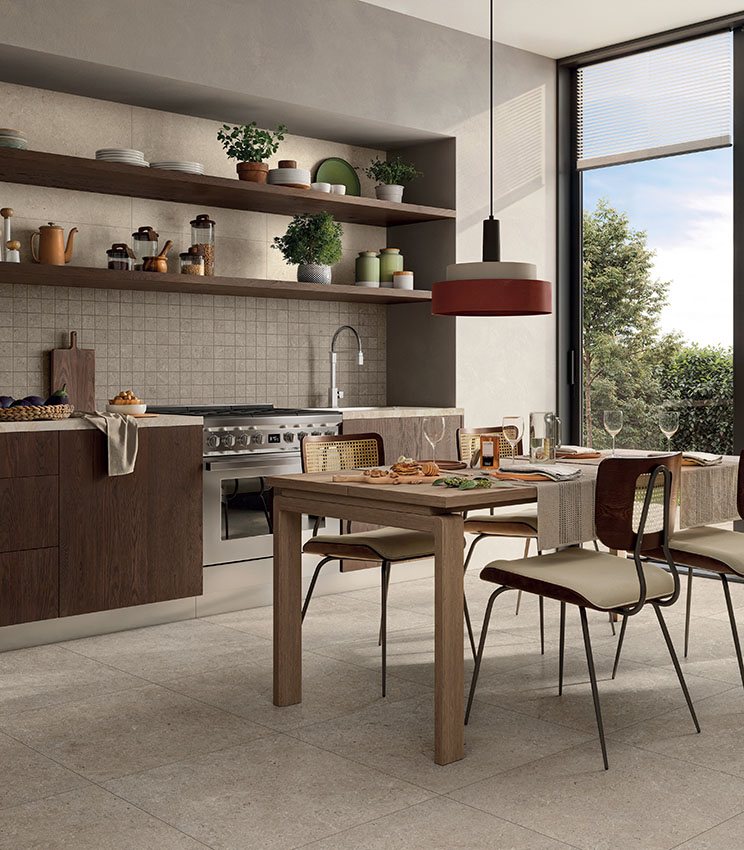 Cuisine moderne avec sol et revêtement mural en carreaux beige effet pierre, mobilier en bois, table à manger et grande fenêtre.