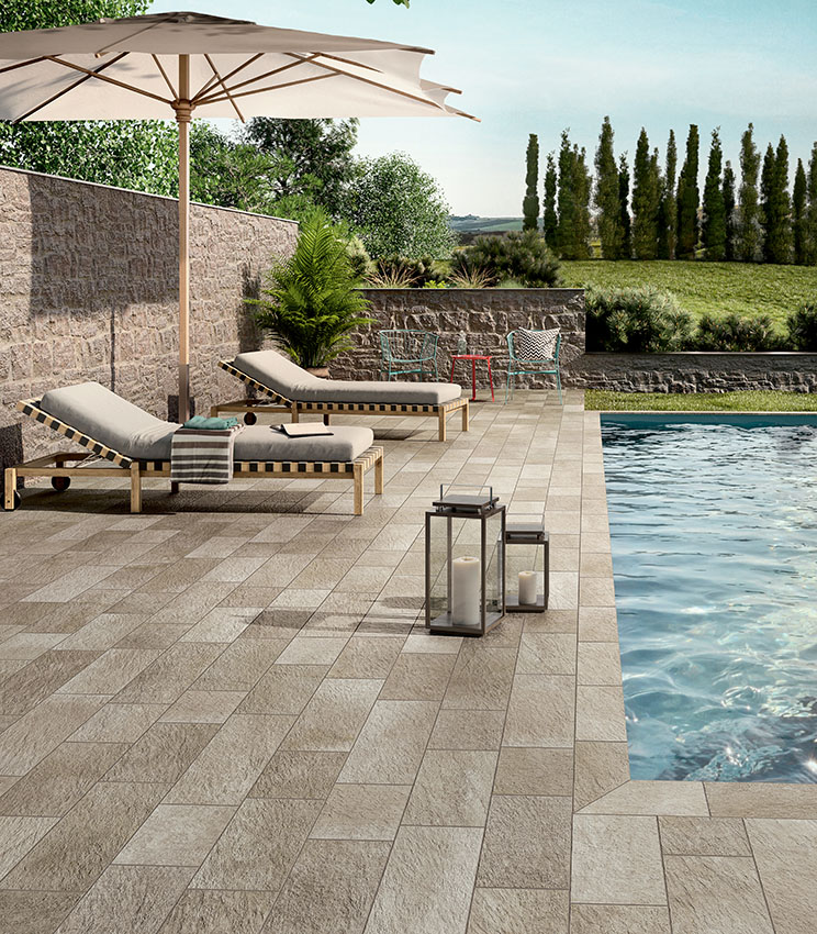 Espace piscine avec sol en grès cérame effet pierre, bains de soleil et mobilier outdoor, pour un environnement élégant, naturel et résistant.