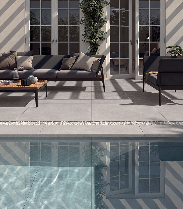 Espace piscine avec sol en grès cérame effet béton, mobilier outdoor contemporain et grandes baies vitrées, pour un environnement élégant et fonctionnel.